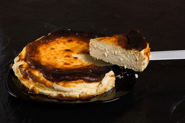 Basque cheesecake on a black plate, on a black slate, one piece was cut off and raised on a knife