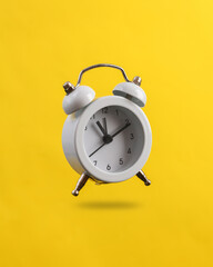 White alarm clock levitating on yellow background with shadow