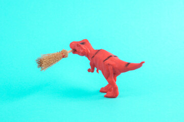 Toy red dinosaur tyrannosaurus rex with halloween witch broom on a turquoise background. Minimalism...