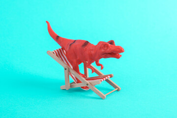 Toy red dinosaur tyrannosaurus rex with deck chair a turquoise background. Minimalism creative layout. Summer rest