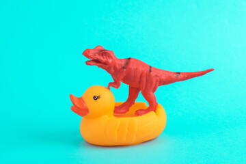 Toy red dinosaur tyrannosaurus rex with rubber duck on a turquoise background. Minimalism creative layout