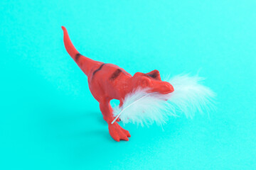 Toy red dinosaur tyrannosaurus rex with soft feather on a turquoise background. Minimalism creative...