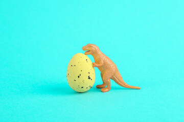 Toy dinosaur tyrannosaurus rex with easter colored egg on a turquoise background. Minimalism...