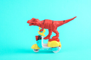Toy red dinosaur tyrannosaurus rex ride on scooter, turquoise background. Minimalism creative...