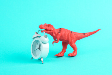 Toy dinosaur tyrannosaurus rex with alarm clock on a turquoise background. Minimalism creative layout