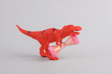 Toy two dinosaur tyrannosaurus rex with hourglass on gray background. Minimalism creative layout