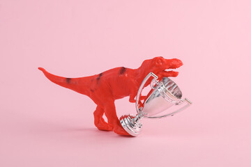 Toy two dinosaur tyrannosaurus rex with winner cup on pink background. Minimalism creative layout