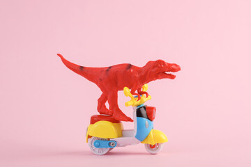Obraz premium Toy red dinosaur tyrannosaurus rex ride on scooter, pink background. Minimalism creative layout.
