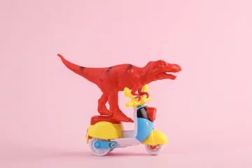 Deurstickers Toy red dinosaur tyrannosaurus rex ride on scooter, pink background. Minimalism creative layout. © splitov27