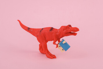 Toy dinosaur tyrannosaurus rex holding house on pink background. Minimalism creative layout