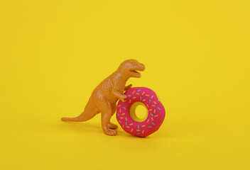 Toy dinosaur tyrannosaurus rex with donut on yellow background. Ninimalism creative layout