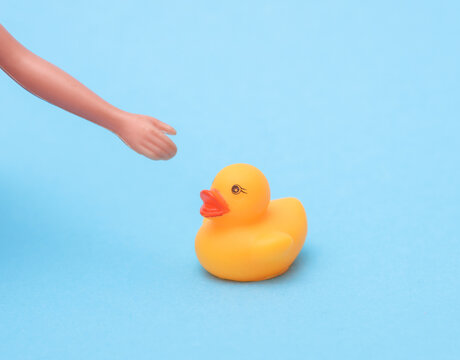 Rubber duck and doll hand on blue background