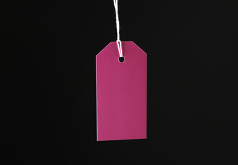 Pink price tag hanging on ropes isolated on black background