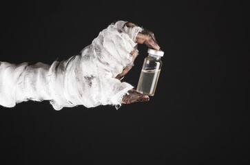 Mummy hand with vaccine bottle isolated on black background. Halloween, gaming concept