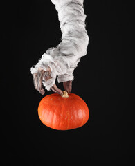 Mummy's hand wrapped in bandage holds pumpkin isolated on black background. Halloween concept