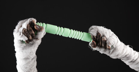 Mummy hand holding pop tube antistress toy isolated on black background. Halloween concept