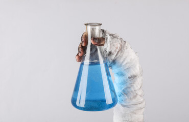 Mummy's hand wrapped in a bandage holds a laboratory flask with blue elixir isolated on a black...
