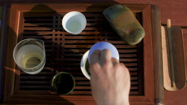 Overhead view of man preparing Oolong green tea on table. Cropped image of male with containers at pier. He is enjoying traditional ceremony during summer weekend. Gaiwan on chaban Chinese tea