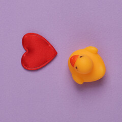 Rubber duck with heart on purple background. Top view
