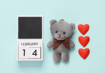 February 14 wooden calendar with teddy bear and hearts on blue background. Valentine's Day