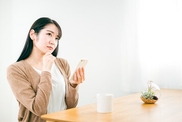 家でスマホのアプリを使いながら考える女性
