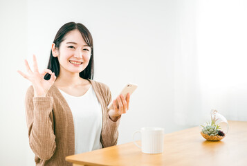 家でスマホを持ってOKサインする日本人女性
