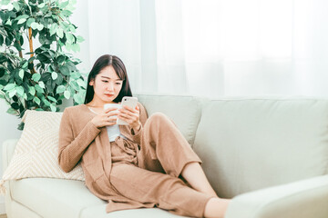 スマホを見てショックを受ける日本人女性（ソファ）
