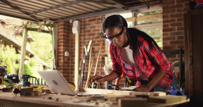 African American female carpenter working with computer laptop in workshop