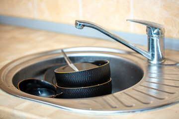 A pile of dirty dishes in the sink. Black dishes are stacked in a metal sink in the kitchen....