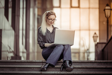 Cute business woman working at a laptop while sitting on the stairs. Lifestyle. Online work