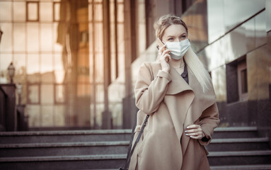 Obraz premium Blond woman in medical mask talking on the phone in the city
