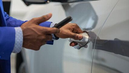 Black salesman opens car using special app for unlocking car on mobile phone. Dealer demonstrates modern technology in automobile salon