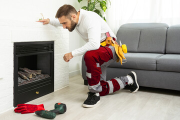 Professional technician sealing electric fireplace near white wall in room