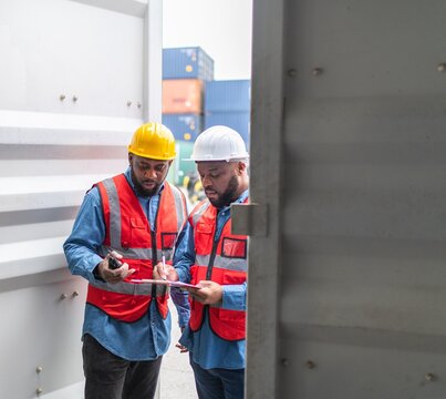 Portrait photo of the moment of two black african male container engineers working and inspecting containers around a shipping yard of a local logistic freight  forwarder company