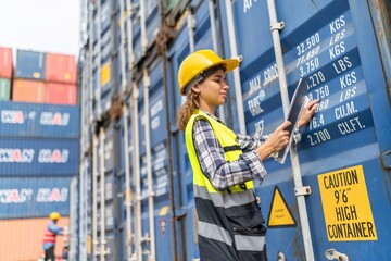 Photo of a young beautiful professional western female brunette engineer inspecting containers in a shipping containers yard to ensure the safety and delivery information is correct