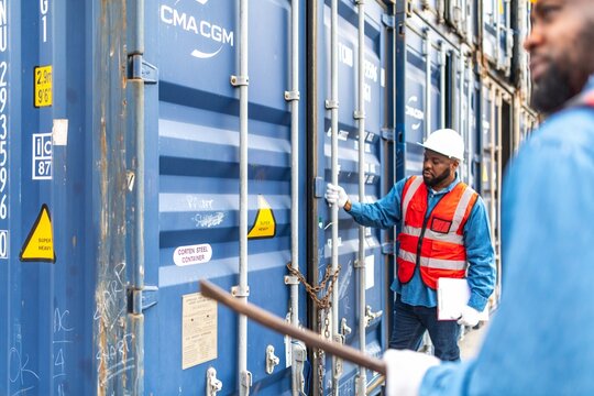Photo of two black african engineer getting ready a crow bar to force open the chain on a container in a shipping containers yard for safety inspection