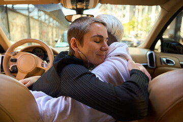 Brunette hugging a blonde in the interior of stylish car