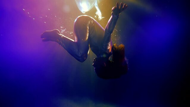 slender woman in silver jumpsuit swims underwater in new cyberpunk style lights