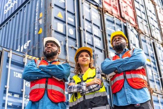Photo of a team of engineers of male and female holding hand together looking front with determination and hope in front a stacks full of containers in a container shipping dock yard