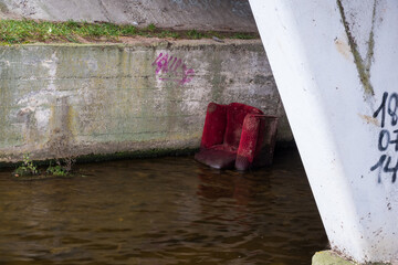 Household garbage in the city. An old torn chair was thrown into a small river, under a bridge.