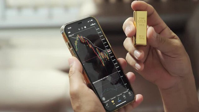 Hand holding gold bars and the phone that opens the candlestick chart. and dollar. Fluctuations in gold prices concept.
