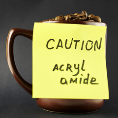 a mug with roasted coffee beans and a yellow sticker on the mug warning about the presence of acrylamide in it