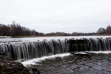 A small man-made waterfall on the lake. Lined with stones, the water froze in flight. Landscape.
