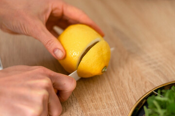 A woman cuts a lemon in half with a knife, hands close-up.Healthy eating and healthy lifestyle.Cooking at home. Vegetarian and vegan diet.Veganuary concept.