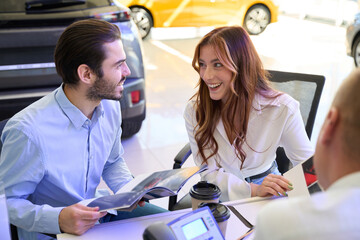 Joyous couple choosing new car model assisted by sales consultant