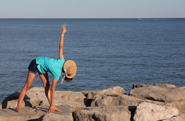 girl in straw hat performs gymnastic exercises by the sea