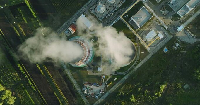 Thermal power plant tower is operating at full capacity in summer and emits steam through chimneys into atmosphere. Energy industry, heat and electricity conversion. Aerial drone view at summer sunset