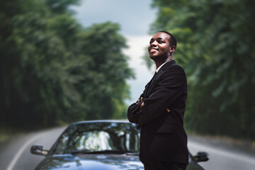 African businessman in a suit driving a car to relax outside of the workplace in the green...
