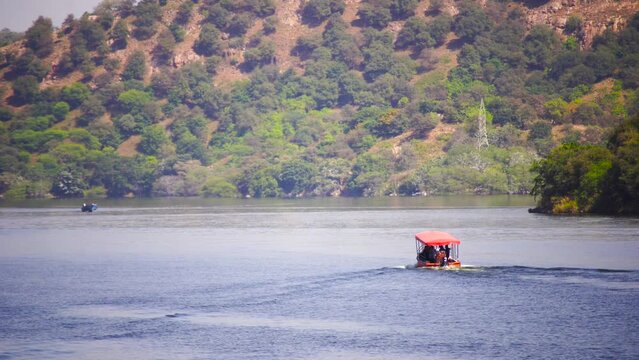 boat moving towards hill covered with trees on asia largest manmade lake Dhebar lake jaisamand udaipur India showing the peace and tranquility of this location