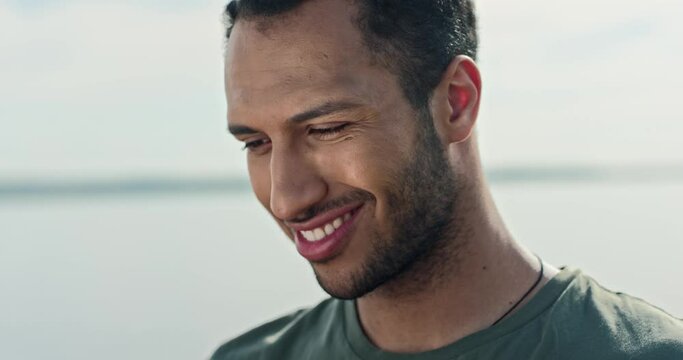 Handsome happy young man tapping on tablet device looking at screen and smiling in good mood. Close up shot of African American male stands outdoors on lake using gadget. Leisure concept
